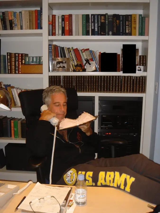 Photograph of Jeffrey Epstein seated in front of bookshelves while holding a telephone and a plate